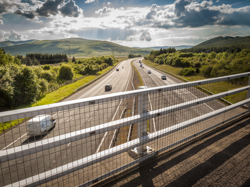 Image from a bridge, looking over metal railing at the highway.
