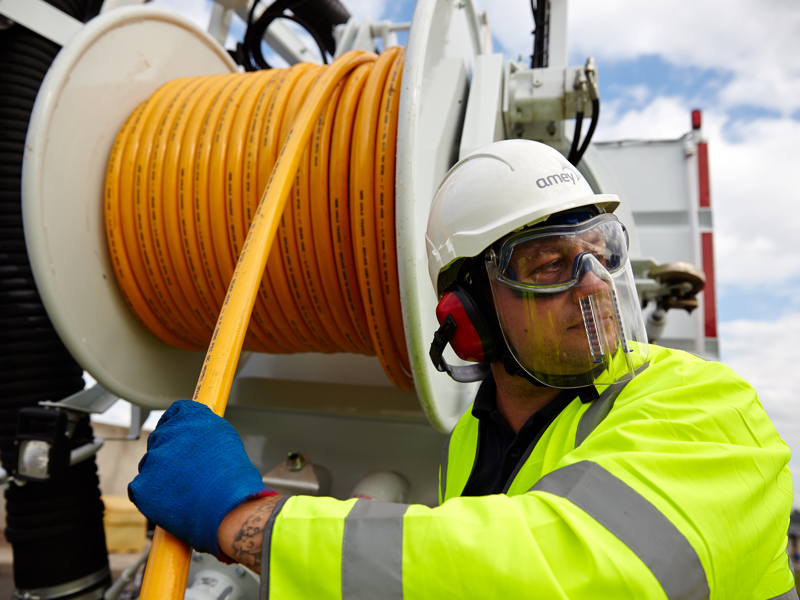 A man in PPE, pulling a hose from a reel.