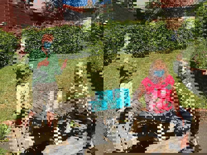 Image of two people on a bench, wearing face masks, donating PPE.