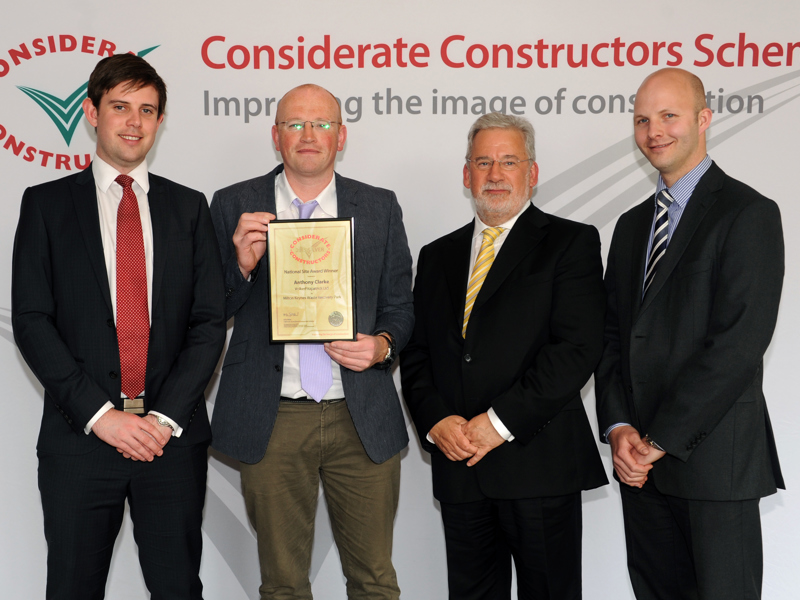 Four men in suits holding a certificate. 