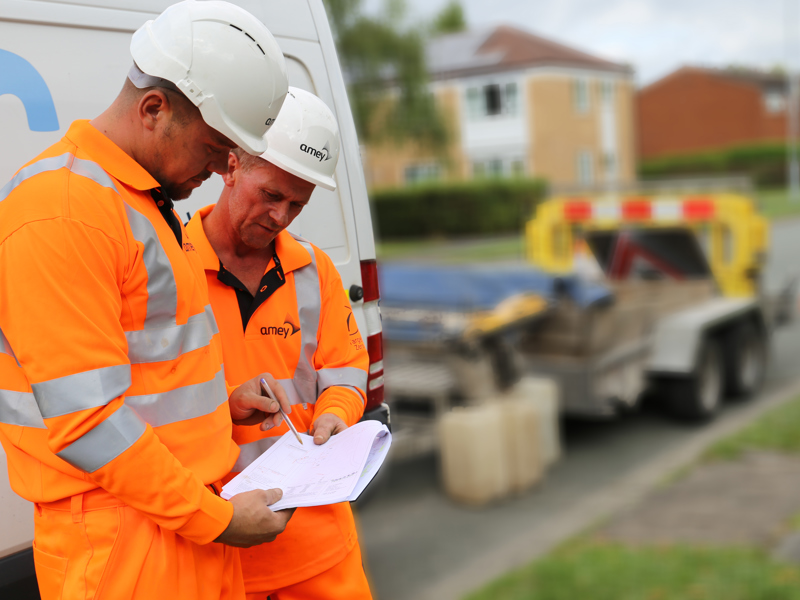 Two men in PPE, inspecting a document.