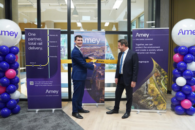 One man cuts an Amey branded ceremonial ribbon while a second man watches. Three Amey branded banners are placed behind them.