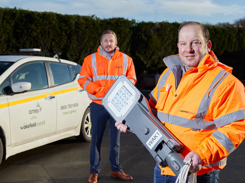 two men in PPE, in front of a car.