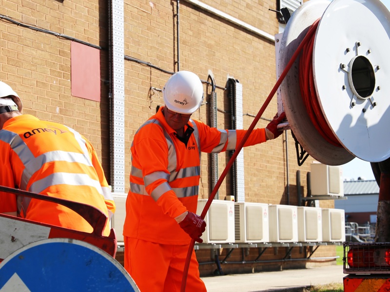 Two men in PPE, pulling a hose from a reel.