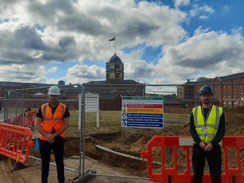 Image of two men stood in front of a fenced off construction area.