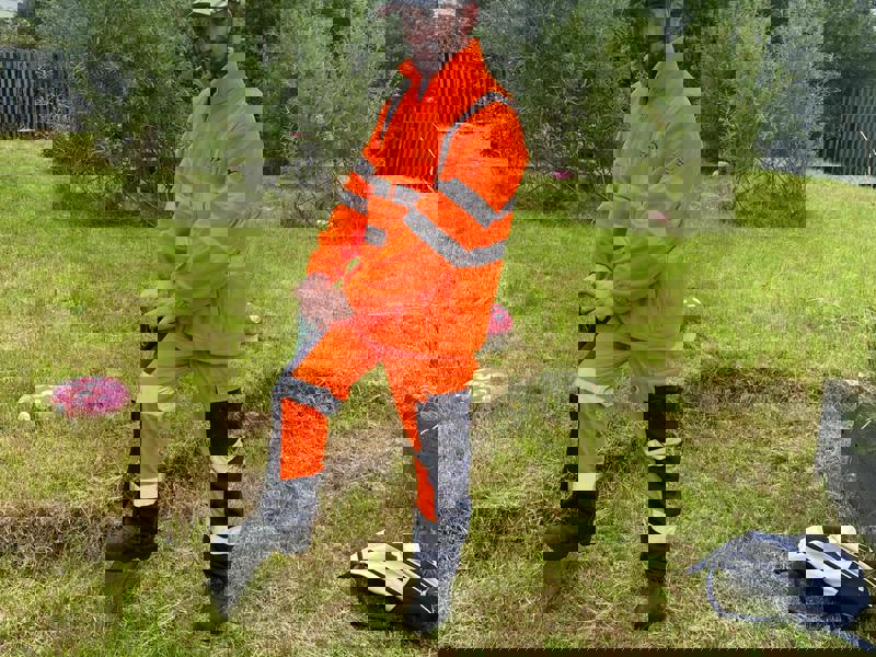 Image of a Amey employee, wearing PPE, stood on a spade in grass.