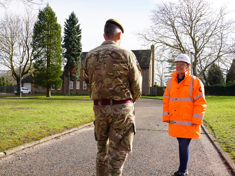 A man in military uniform stands facing a woman in orange PPE