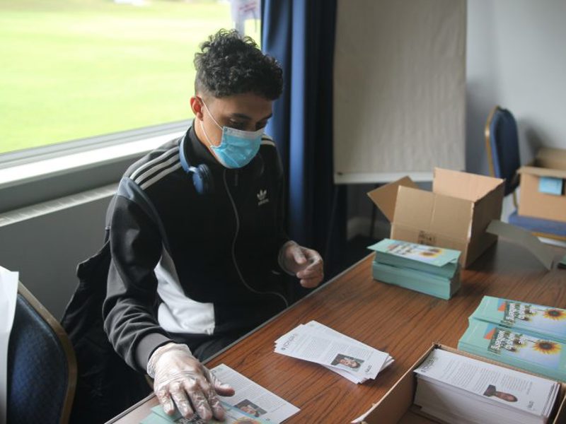A man at a desk, wearing a face covering.
