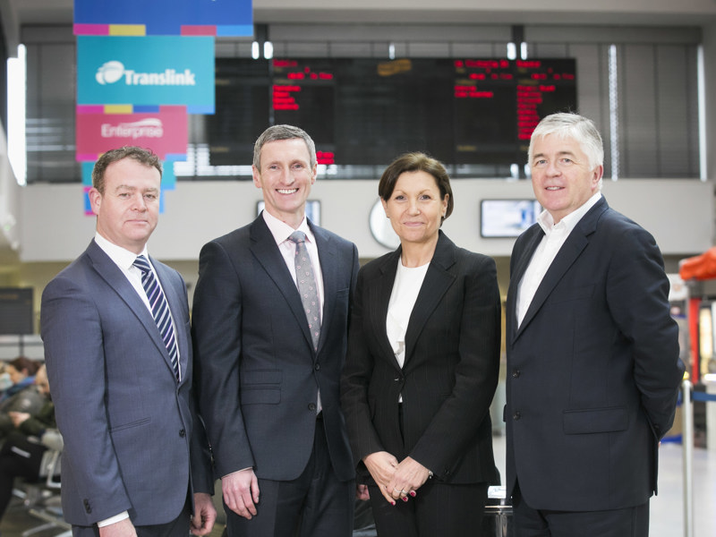 Group of four people stood in front of a departure board at a train station.