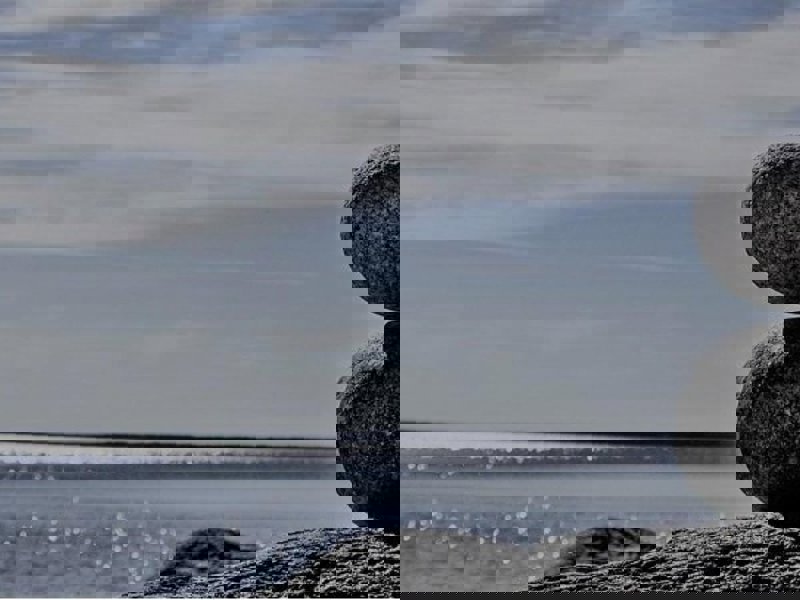 Image of two pebbles balancing on top of each other at a beach.