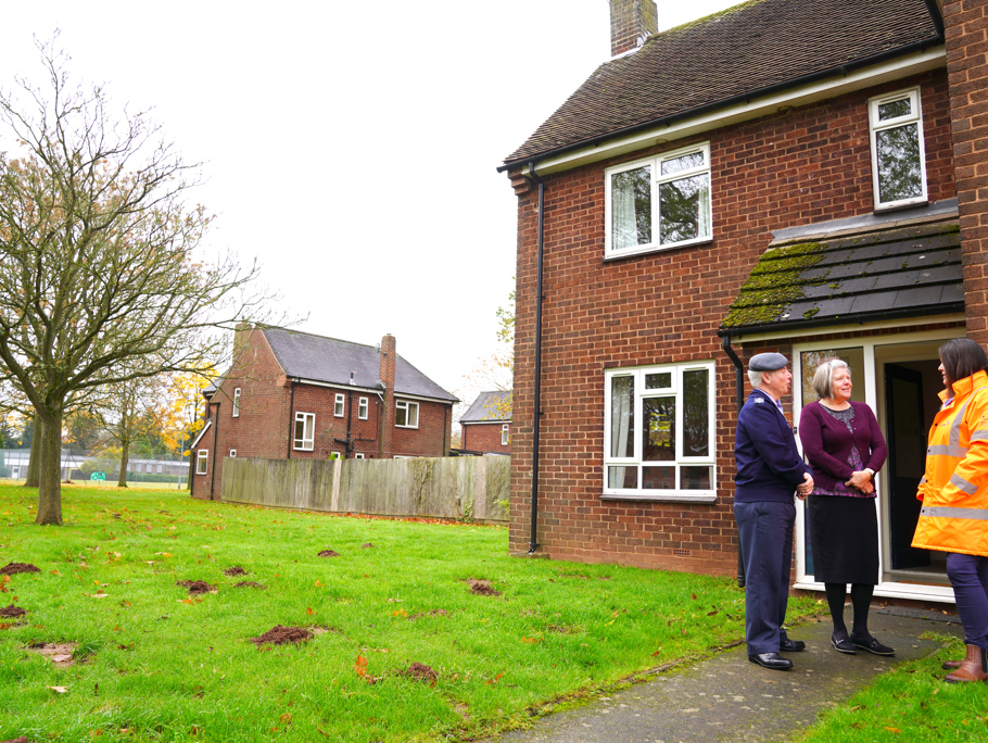 Image of military personnel and an Amey employee standing in front of a house.
