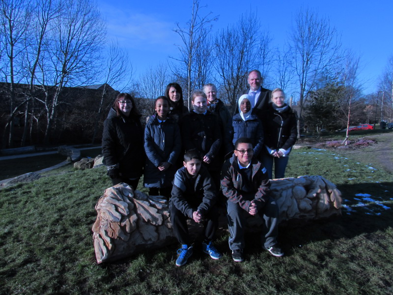 A group of school students sat on a tree carving. 