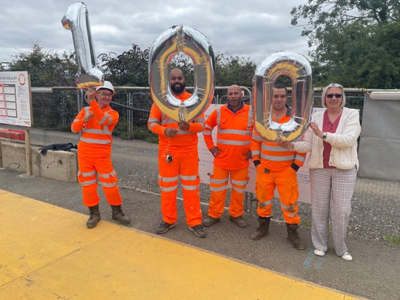 a group of people holding '100' number balloons.