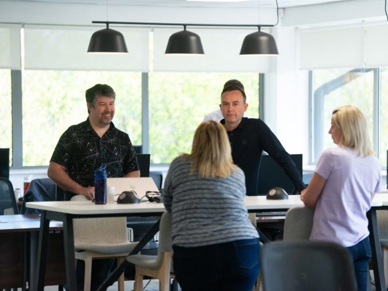 Two men and two women, stood at opposite sides of a desk.
