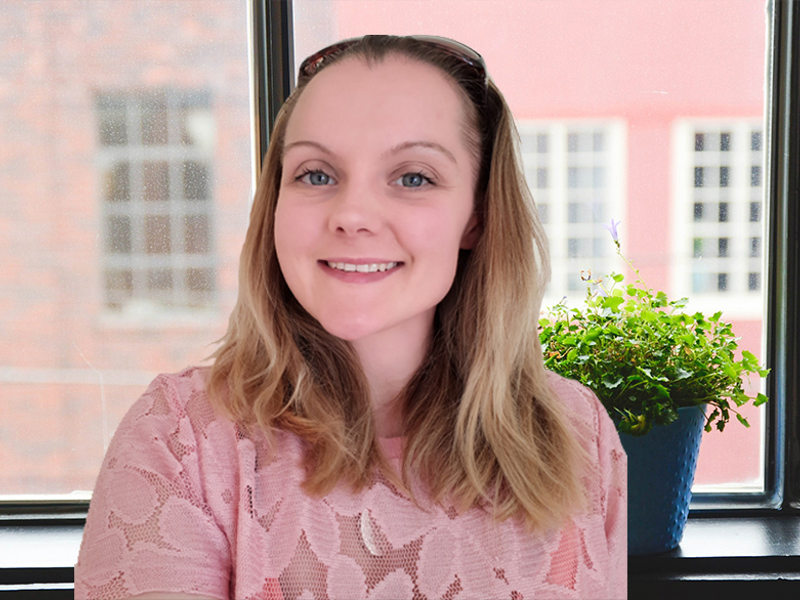 Image of a woman stood in front of a window with a potted plant.