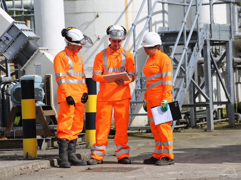 Image of three Amey employees, wearing PPE inspecting a document.