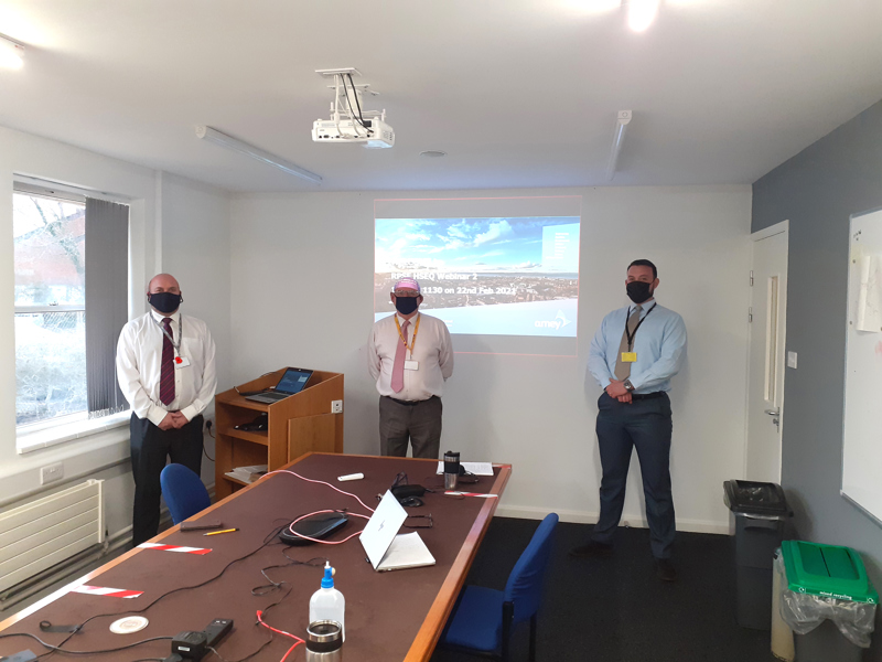 Image of three men, in face masks, practicing social distancing in an office.