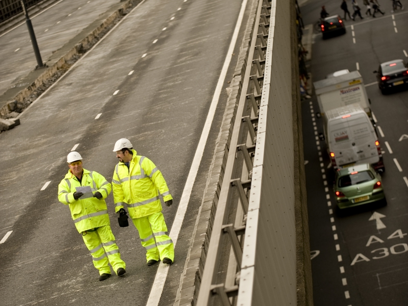 Two males in PPE walking across a bridge.