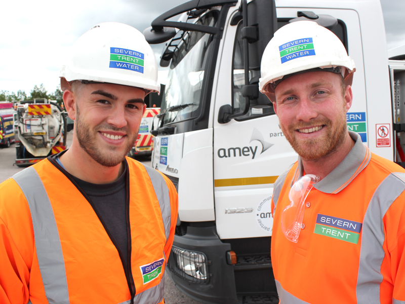 Two men in PPE, stood in front of a van.